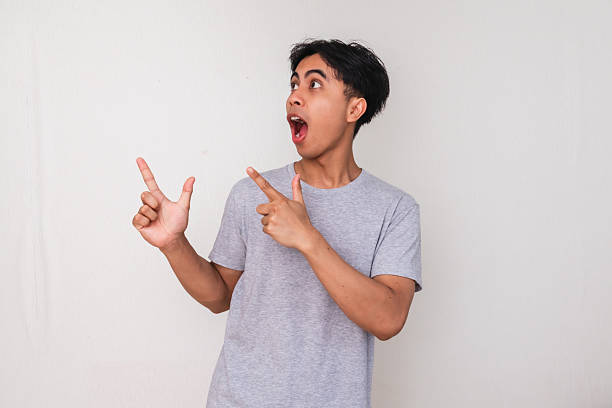 istock Portrait of a young Asian man pointing sideways with a funny wow expression on face, isolated on white background, perfect for promotion or advertisement content 2222689720