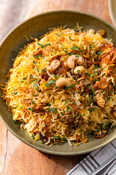 Indian Chicken biriyani rice dish served in restaurant with cashew nuts, raita yoghurt sauce and papadum bread