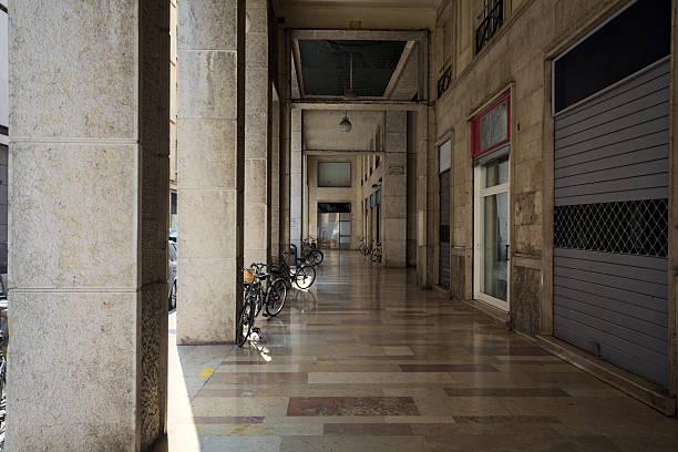 Tall and narrow porch under a building with closed shops and bicycle leaning on the columns