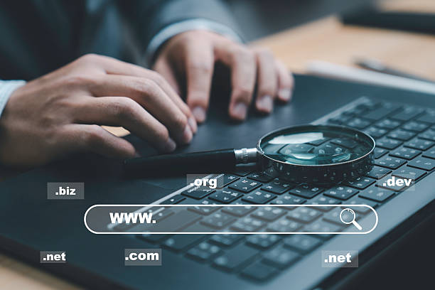 istock A close-up of hands typing on a laptop keyboard, showcasing various domain extensions such as .com, .net, and .org. The magnifying glass indicates searching for information online. 2222711599