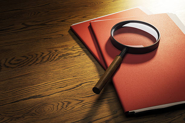 Magnifying glass on red confidential folders placed on dark wooden desk under spotlight viewed from top with luxury business investigation concept.. 3D Rendering