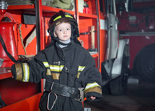 istock Serious little boy in firefighter uniform at fire station 2222713956