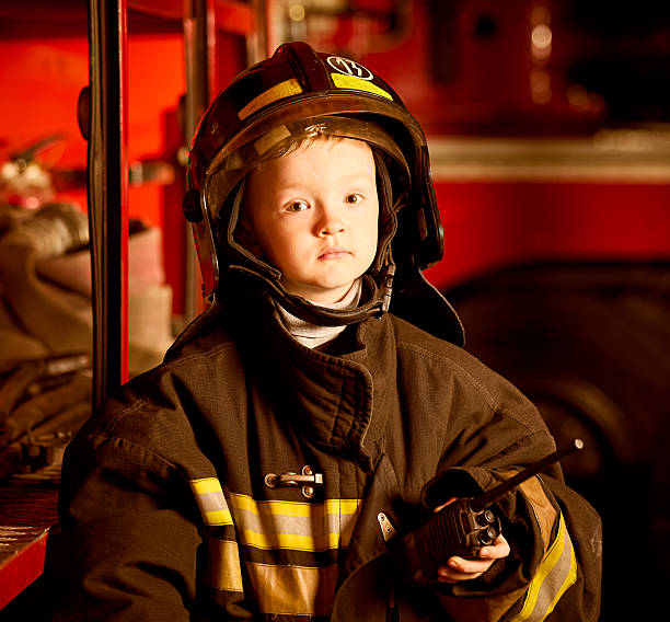 istock Cute boy in firefighter clothes at stand with firefighting equipment 2222713963
