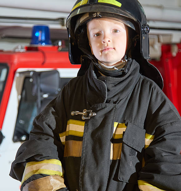 istock Funny kid firefighter in protective firefighting clothing standing in a fire station 2222714012