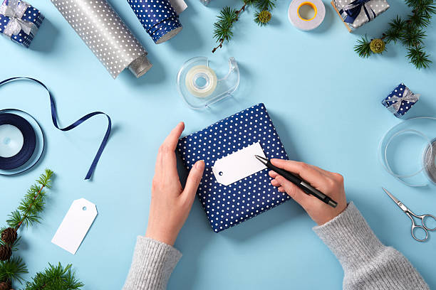 istock Hands write on a gift label. Around it are ribbon, scissors, tape, spruce twigs, and small wrapped gifts. Preparing for the holidays. 2222716975