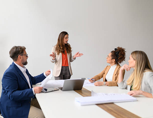 istock Female entrepreneur with laptop and blueprints on table discussing ideas and plans with coworkers in office during meeting 2222718467