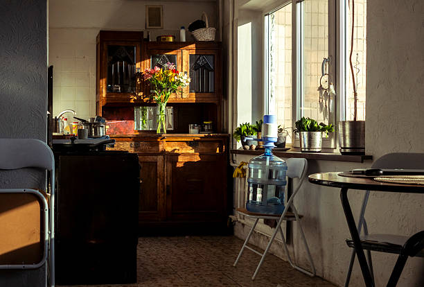 Modern kitchen interior featuring black dining table with four chairs, wooden cabinets, black tile backsplash, built-in microwave, vase with dried flowers on table, no people visible