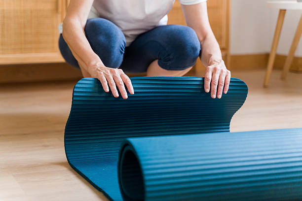 istock Woman rolling a blue yoga mat at home 2222725279