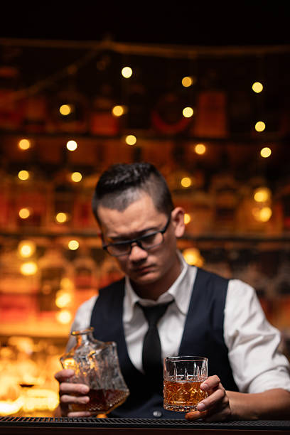 Handsome businessman or young man sits, drinks whiskey, looks stressed and sad.