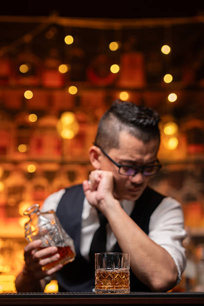 Handsome businessman or young man sits, drinks whiskey, looks stressed and sad.