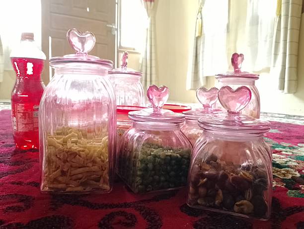 A vibrant composition showcasing an assortment of snacks, including lentils, peas and chickpea, and red syrup, stored in elegant glass jars adorned with heart-shaped lids. This image captures the essence of homemade treats and thoughtful food storage.