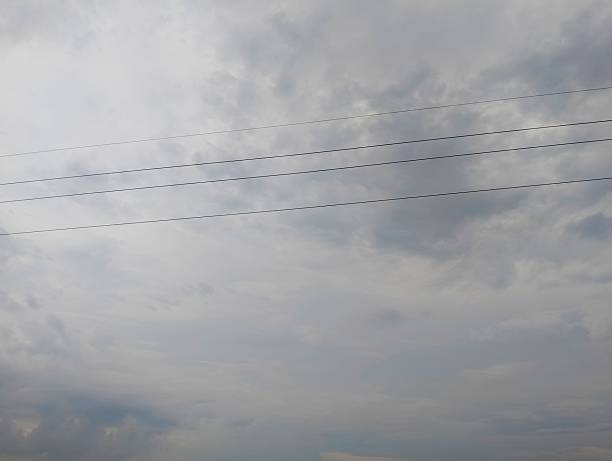 A view of power lines silhouetted against a cloudy sky. The scene suggests an overcast day, possibly hinting at an approaching storm. The transmission lines stretch across the horizon, carrying electricity through the infrastructure.