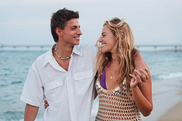istock Joyful couple enjoying a lively stroll on a beautiful beach while holding hands and sharing smiles under the soft glow of the early evening sun near the calming sea and gentle waves 2222737416