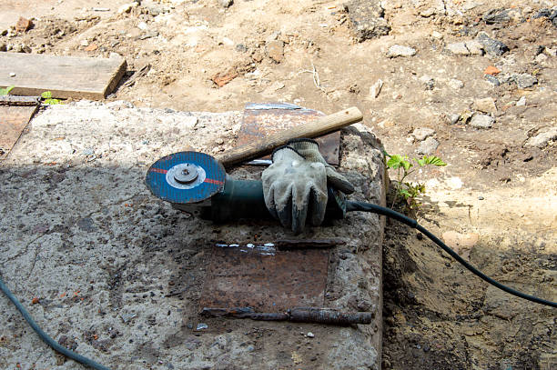 A circular saw rests on a worn concrete slab surrounded by dirt and debris, indicating ongoing renovation at a construction site.