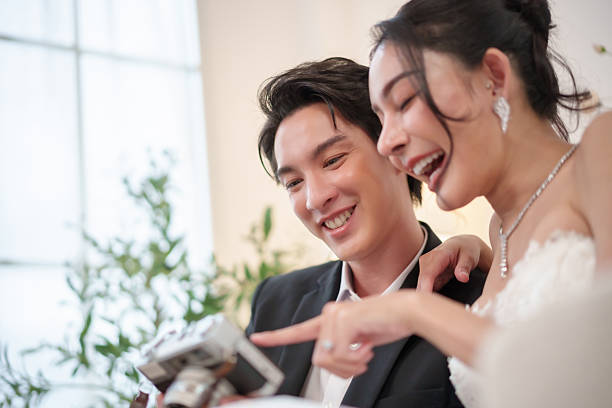 Asian Couple laughing together while checking photos at camera. Pure joy and connection in their wedding moment.