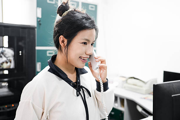 Young hotel receptionist in suit and tie answers a landline phone at the front desk, smiling and professionally assisting a guest with check-in and customer service needs