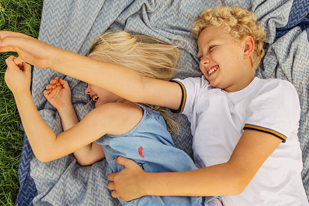 istock Two children lying on a blanket outdoors laughing and enjoying a playful moment 2222751212