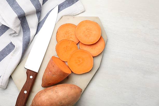 istock Fresh sweet potatoes, knife and kitchen towel on white table, flat lay. Space for text 2222754064