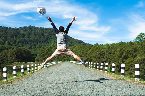 Man happily jumping with arms raised on a country road. Symbolizes freedom, joy, travel, and adventure in nature.