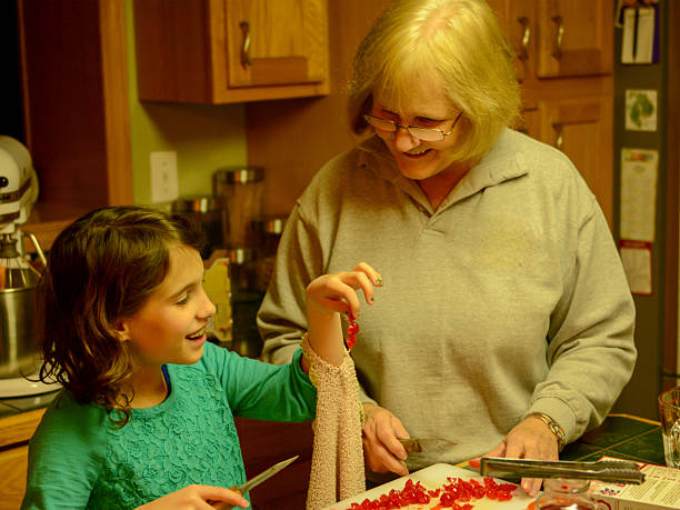 A warm, cozy domestic scene where a woman guides two children as they prepare soup at a wooden table. Christmas lights glow softly in the background. Vintage camera filter.