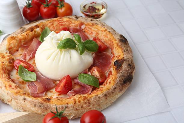 istock Delicious pizza with burrata cheese, basil, tomatoes and ham on white tiled table, closeup 2222755892