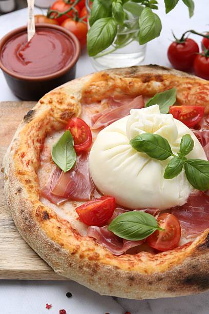 istock Delicious pizza with burrata cheese, basil, tomatoes and ham on table, closeup 2222755893