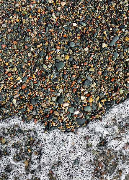 Seafoam lapping at pebble covered shore. Natural sea texture, suitable for backgrounds, vacation themes, nature, travel.