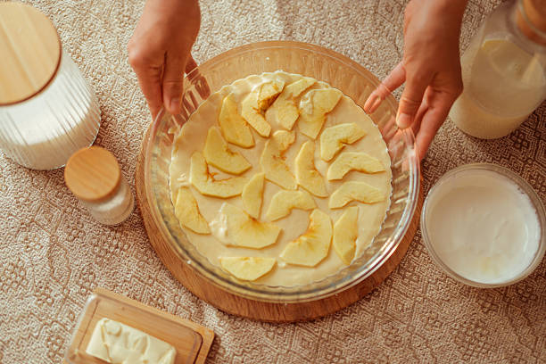 istock A top-down view shows a cook's hands holding a glass pie dish filled with batter and arranged apple slices, ready for baking. 2222765307