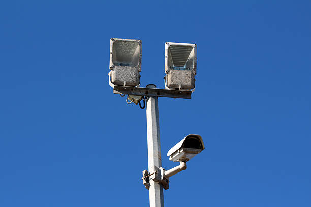 istock Security floodlights and surveillance camera mounted on pole against blue sky 2222774150