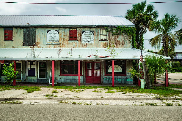 Formerly a building with several businesses but now empty, abandoned and dilapidated, American flags in the front door windows.  Located in the Florida gulf coast town of Apalachicola, this photo was taken on July 12, 2019.