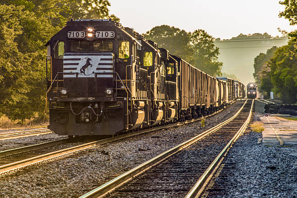 Two sets of railroad tracks, each with an oncoming train,  late afternoon, low sun angle, hazy air down the tracks in the distance.