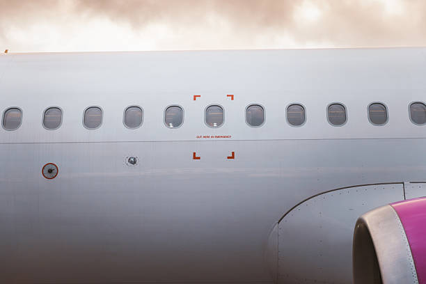 Close-up detail of the side of a passenger aircraft showing cabin windows and the clearly marked emergency exit zone. The image features clean design lines and aviation safety elements, creating a sleek, modern visual suitable for editorial and commercial use.