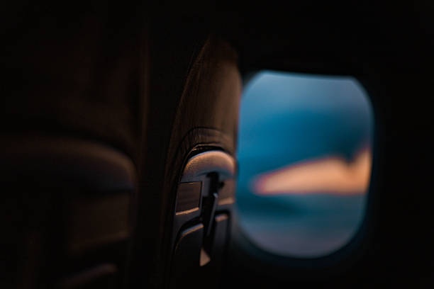 A dreamy view of an airplane wing captured through the passenger window during a colorful sunset. The soft light, pink streaks in the sky, and fluffy clouds create a tranquil and cinematic flying atmosphere from inside the aircraft.