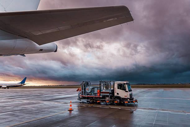 Ground support equipment parked on the wet tarmac of an airport during sunrise. A dramatic sky and aircraft in the background highlight the logistical operations and infrastructure behind modern aviation.