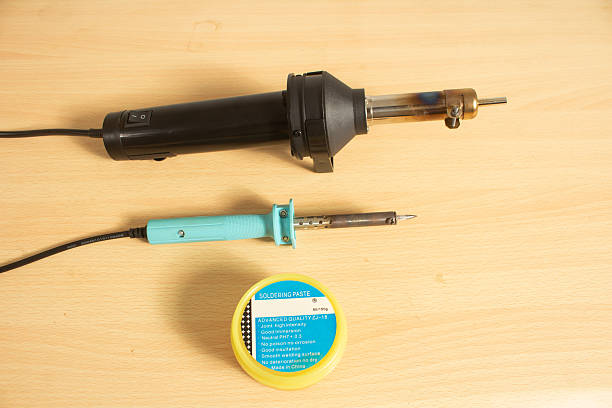 Torquoise colored soldering iron black colored heat gun isolated neutral background power cable soldering paste