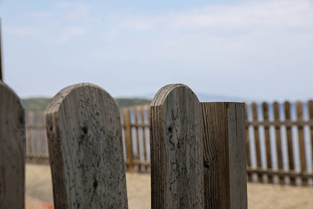 Close-up of a rustic wooden fence with the calm sea in the background. The image evokes themes of solitude, nature, and boundaries, with a soft horizon and neutral tones ideal for background or concept use.