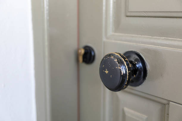 Close-Up Of A Worn Vintage Door Handle On A Painted Wooden Door. The Black Doorknob Shows Signs Of Age And Use, With Paint Peeling Off, Adding A Rustic And Nostalgic Touch. Interior Detail In An Old Building Or Home.