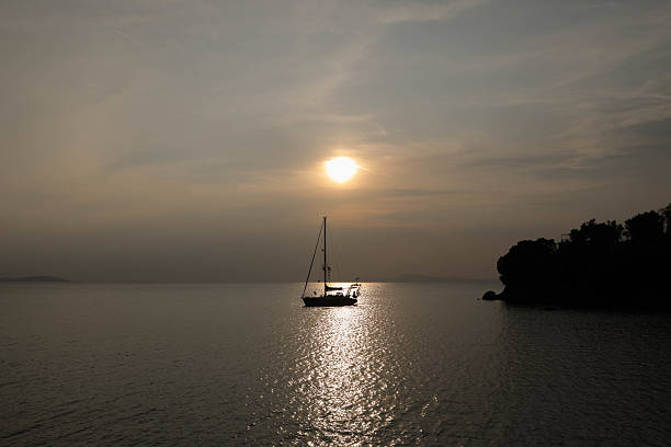 Scenic view of a sailboat peacefully floating on the sea at sunset. The warm golden light reflects off the water, creating a tranquil and romantic atmosphere. Perfect for concepts of freedom, travel, and serenity.