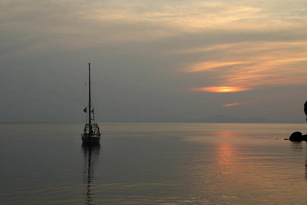A tranquil sailboat floats on calm water at sunset, with soft pink and blue hues reflected on the sea. This peaceful coastal scene evokes freedom, serenity, and luxurious escape, perfect for travel and lifestyle themes.