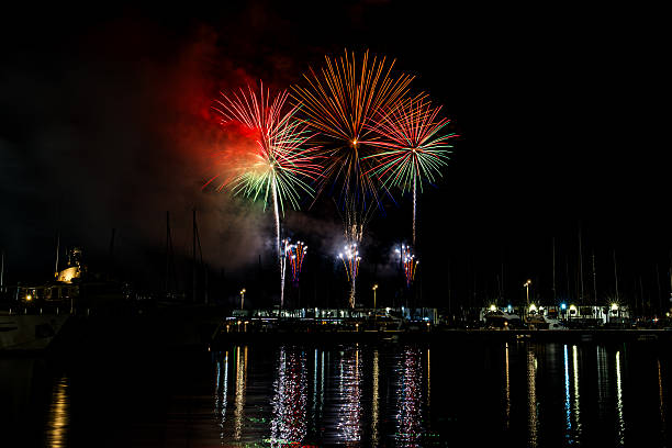 istock Colorful fireworks exploding over a marina at night, reflected in the calm harbor water with yachts and masts silhouetted under a starless sky with copy space 2222793079