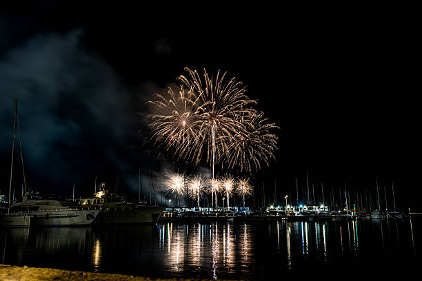 istock Colorful fireworks exploding over a marina at night, reflected in the calm harbor water with yachts and masts silhouetted under a starless sky with copy space 2222793144