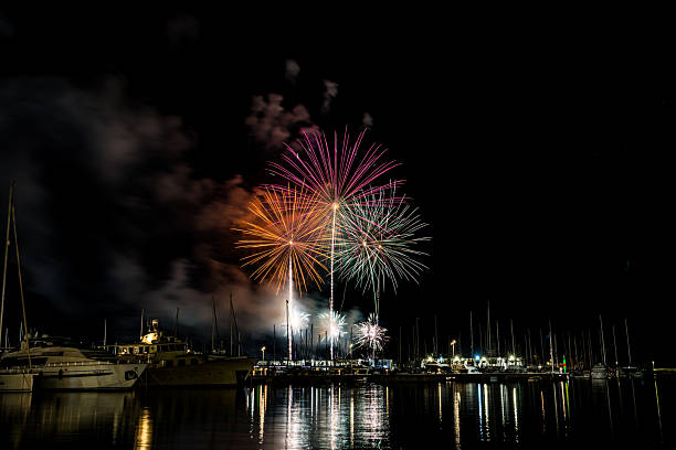istock Colorful fireworks exploding over a marina at night, reflected in the calm harbor water with yachts and masts silhouetted under a starless sky with copy space 2222793193