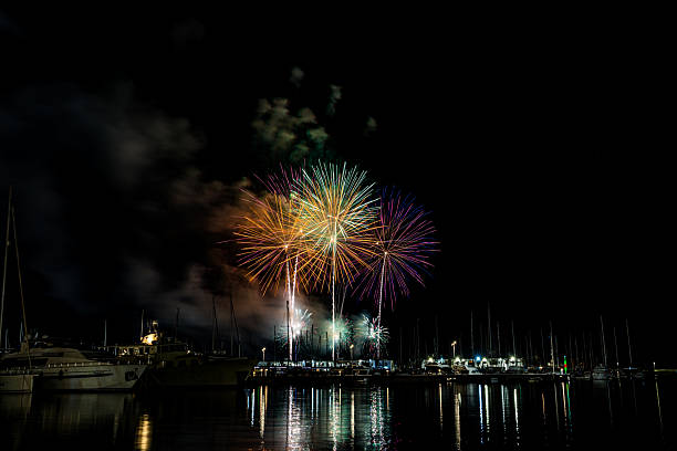 istock Colorful fireworks exploding over a marina at night, reflected in the calm harbor water with yachts and masts silhouetted under a starless sky with copy space 2222793198