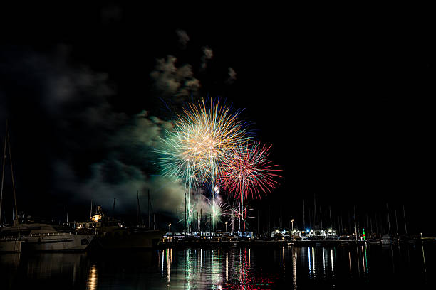 istock Colorful fireworks exploding over a marina at night, reflected in the calm harbor water with yachts and masts silhouetted under a starless sky with copy space 2222793209