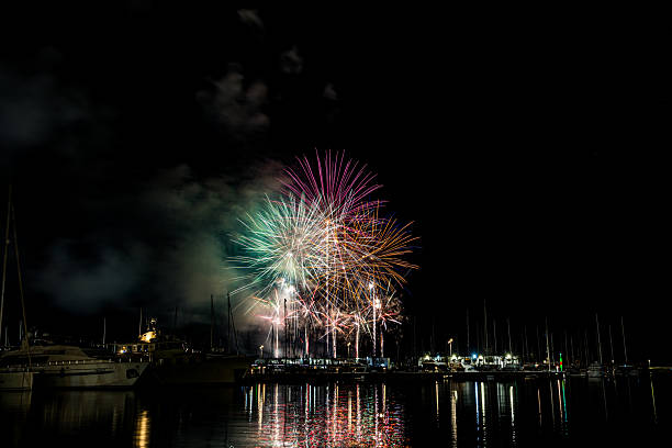 istock Colorful fireworks exploding over a marina at night, reflected in the calm harbor water with yachts and masts silhouetted under a starless sky with copy space 2222793215