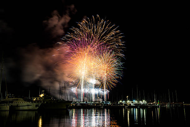 istock Colorful fireworks exploding over a marina at night, reflected in the calm harbor water with yachts and masts silhouetted under a starless sky with copy space 2222793223