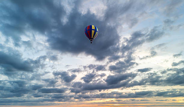istock Colorful hot air balloon flying through dramatic cloudy sky at sunset 2222795317