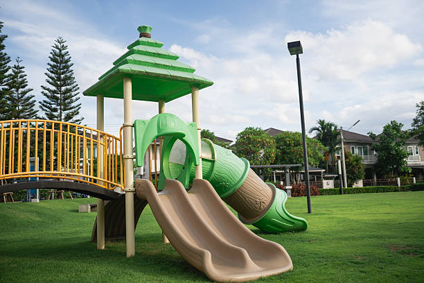 istock Colorful playground structure featuring green slides and climbing area, set in a lush green park with trees and blue sky in the background 2222814026