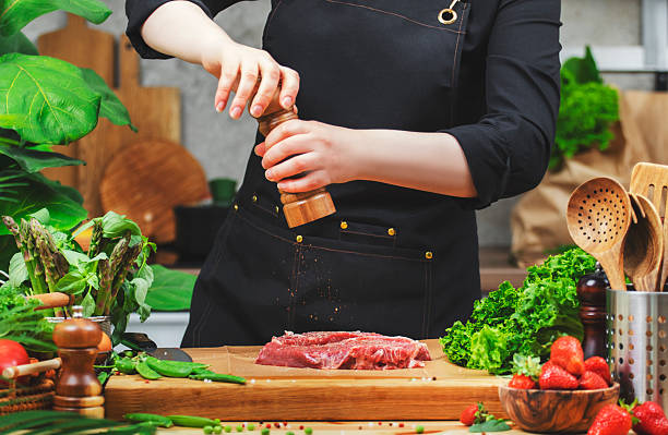 istock chef sprinkle beef steak with pepper from the mill prepares a healthy dish in a cozy kitchen, using fresh farm herbs and vegetables 2222814127
