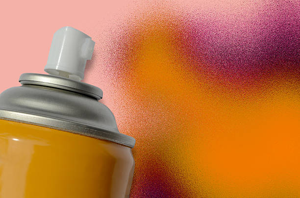 a yellow spray paint can with a background of colorful paint spray spilled on a pink surface